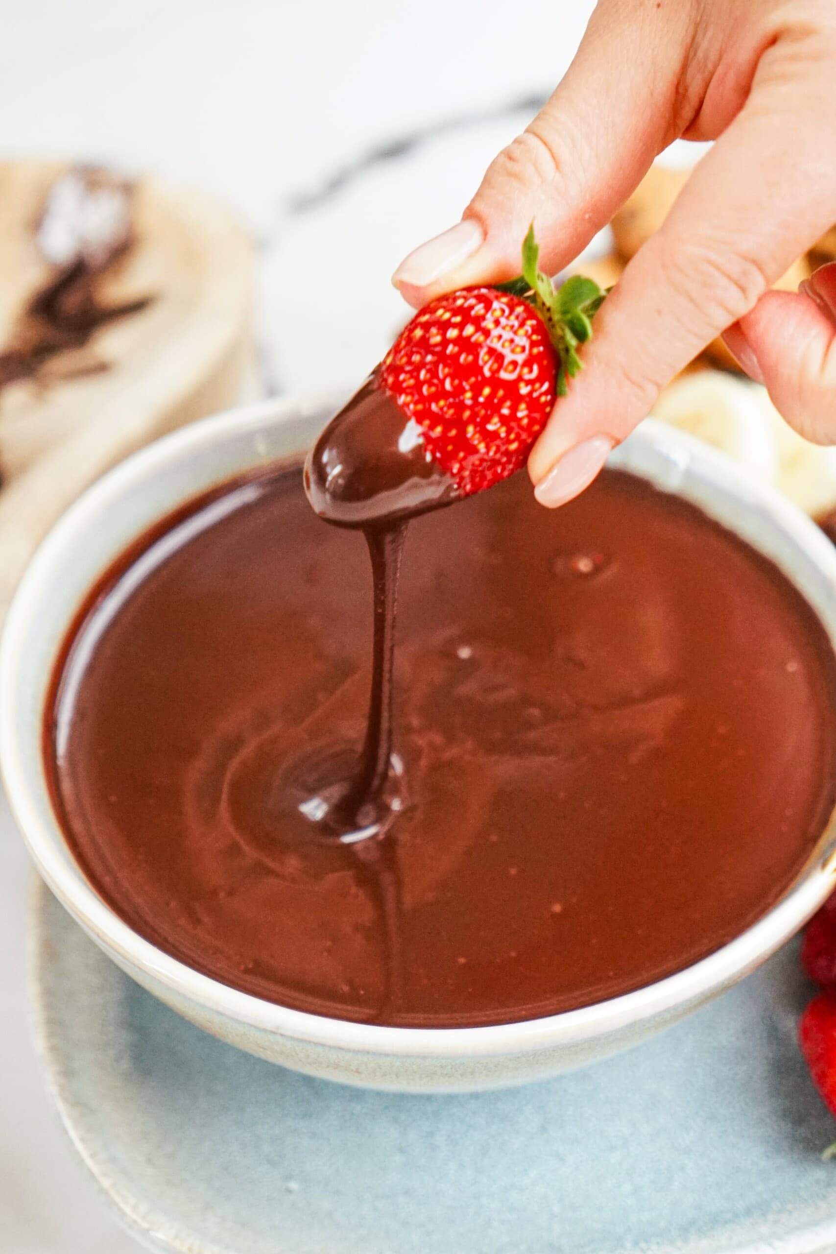 woman's hand dipping a strawberry into a bowl of chocolate.