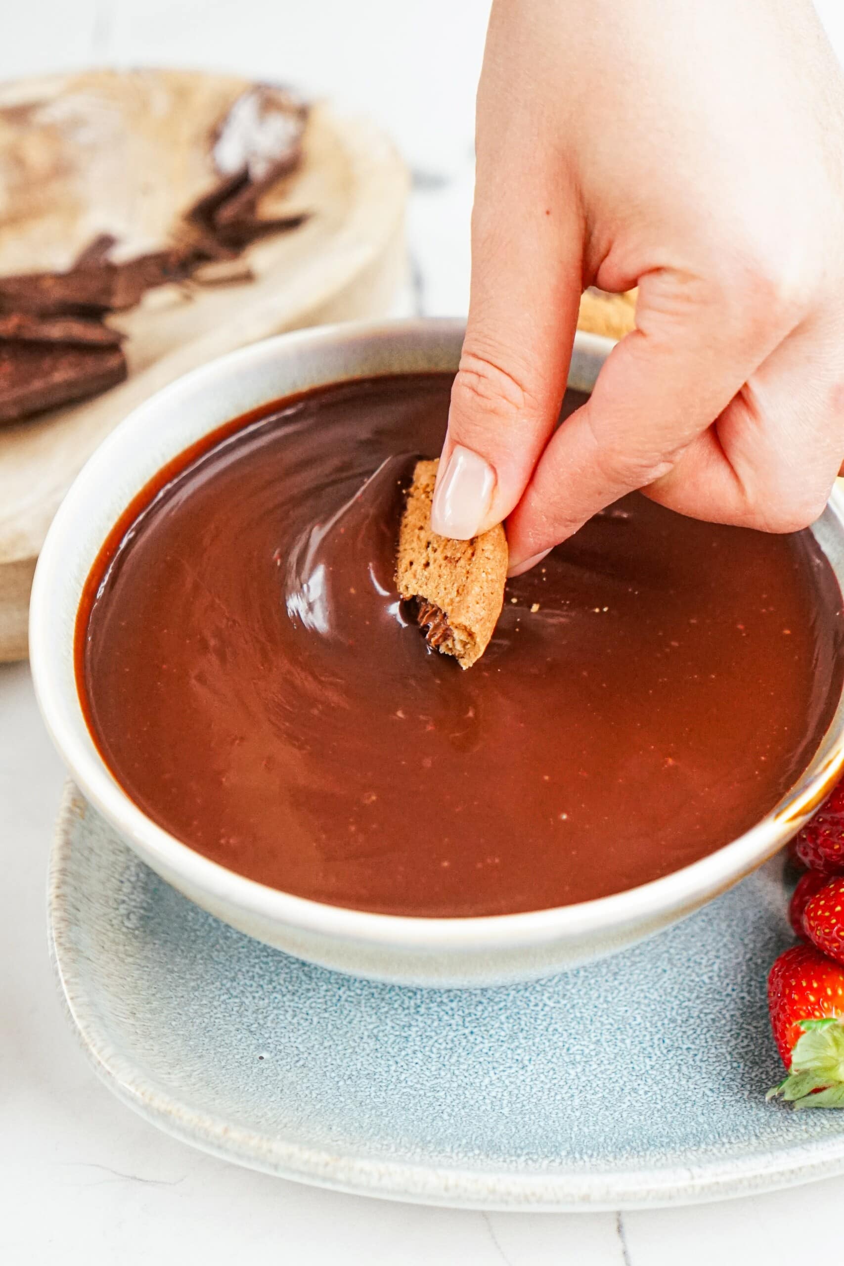 woman's hand dipping a piece of cookie into a bowl of chocolate.