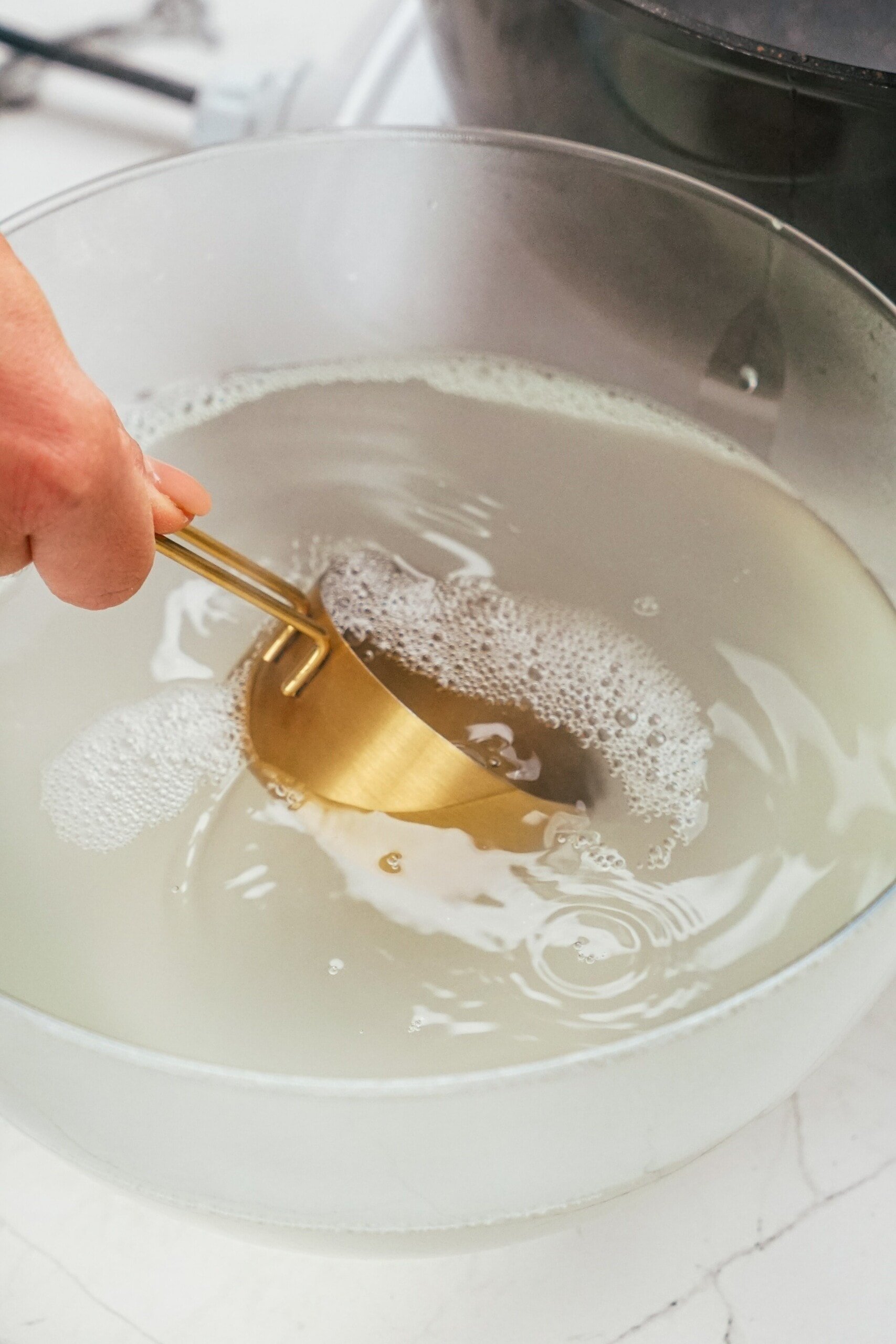 woman's hand dipping measuring cup into reserved pasta water
