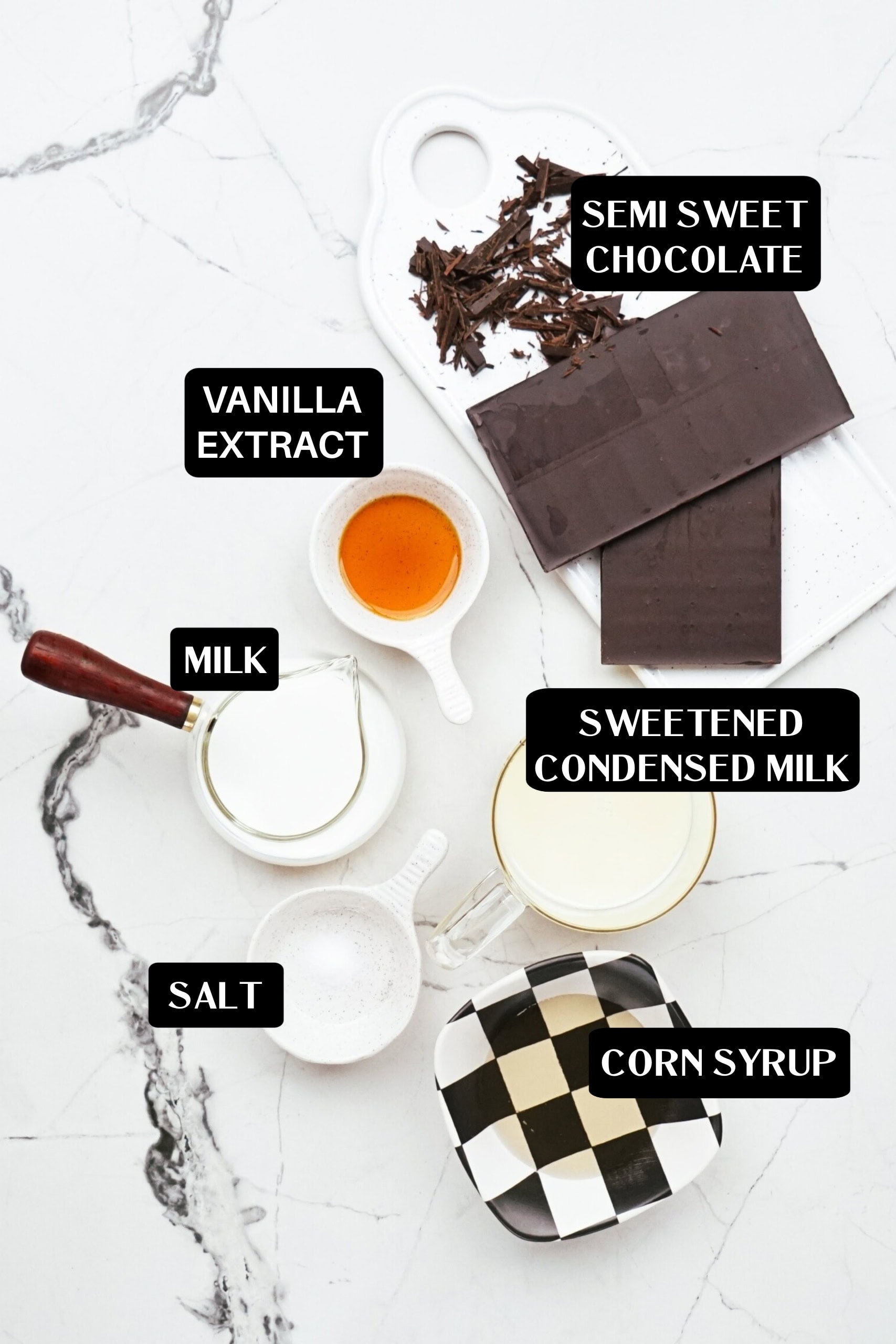 Ingredients for Dipping Chocolate are laid out on a marble surface: semi-sweet chocolate, vanilla extract, milk, sweetened condensed milk, salt, and corn syrup, each labeled.