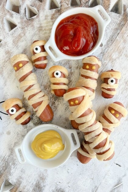 Mummy Dogs on white wooden board with ketchup and mustard