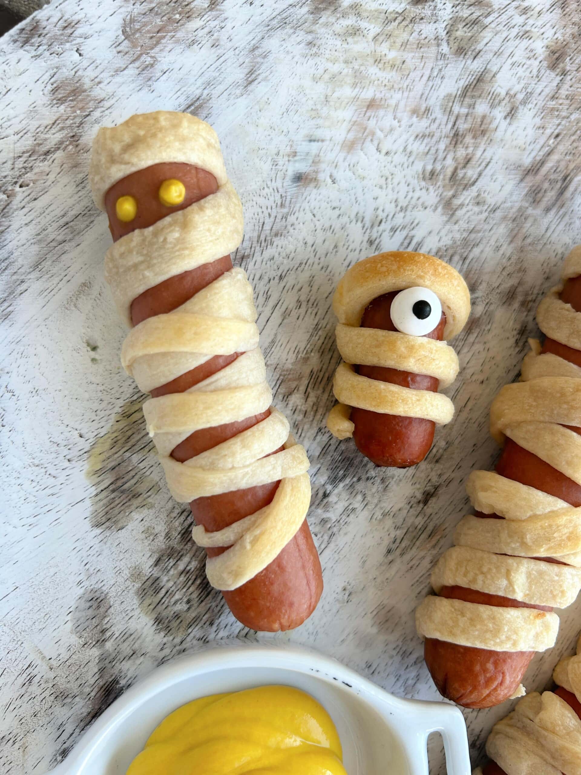 Mummy Dogs on white wooden board with mustard