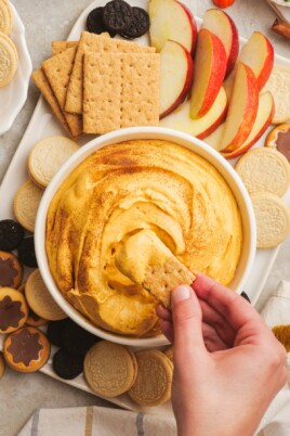 pumpkin dip and a woman's hand dipping cookie into the dip