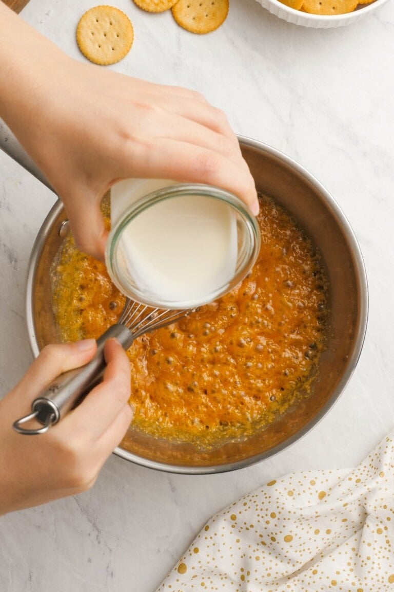 woman's hand adding heavy cream to saucepan