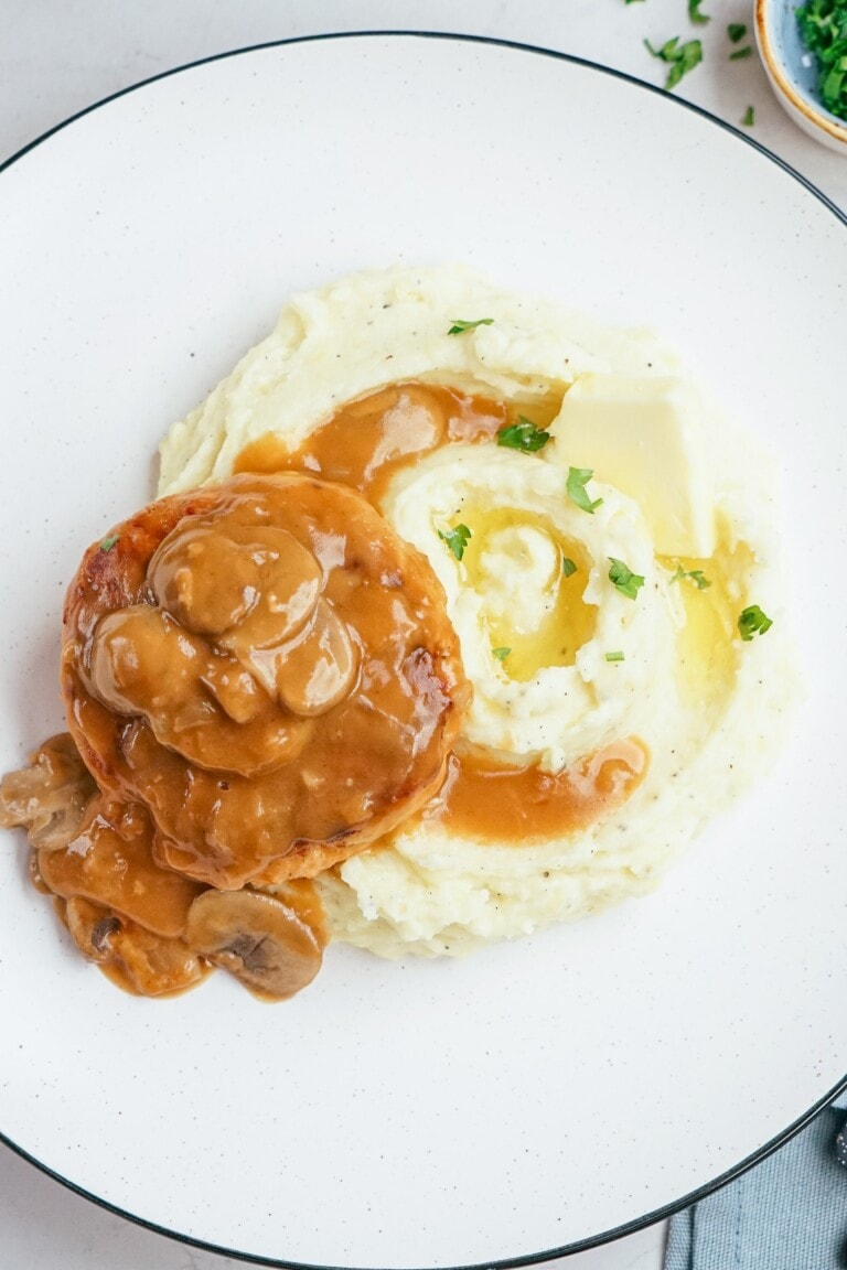 salisbury steak and mashed potatoes on a plate with mushroom gravy poured over the top