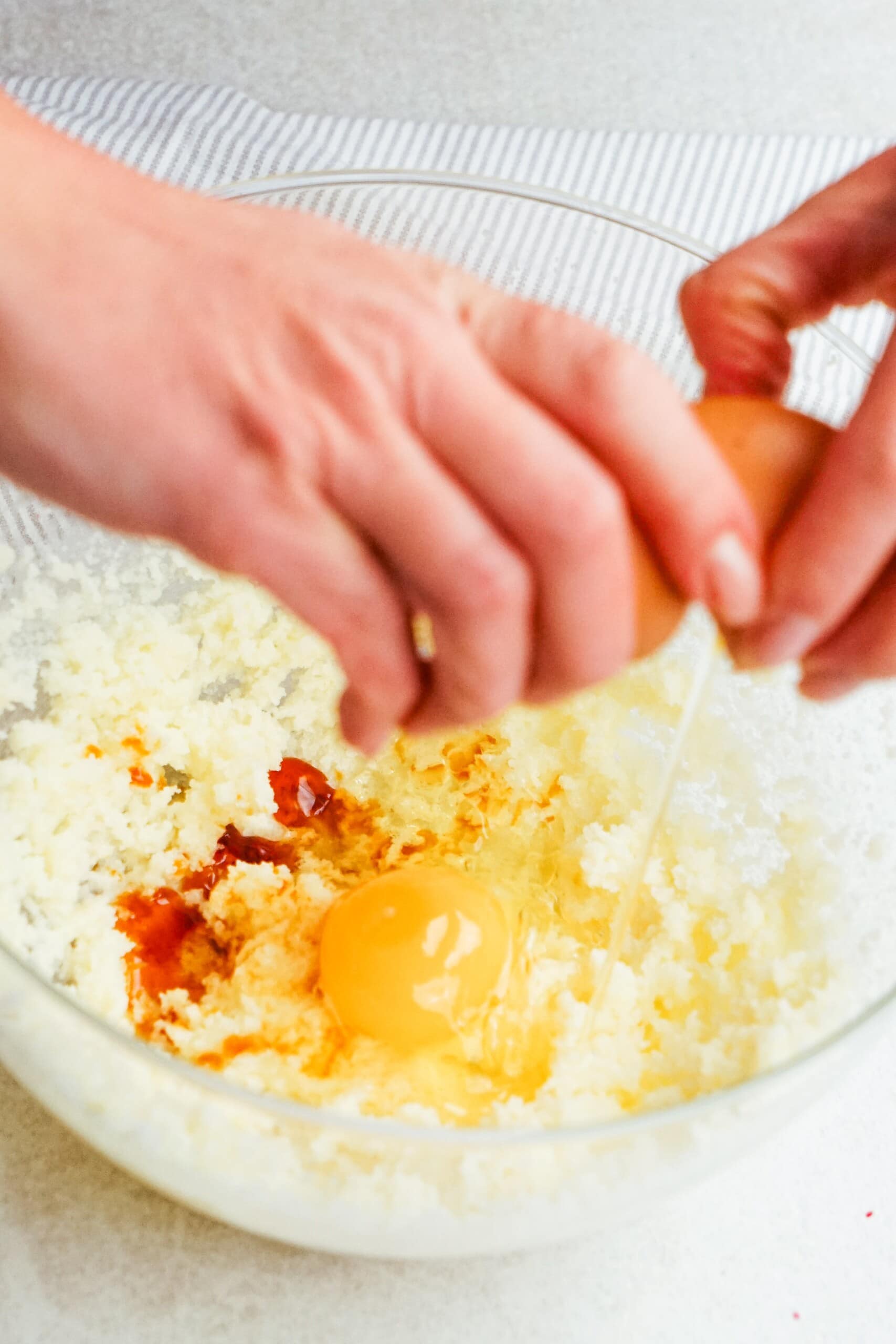 woman's hand cracking an egg into the butter mixture 