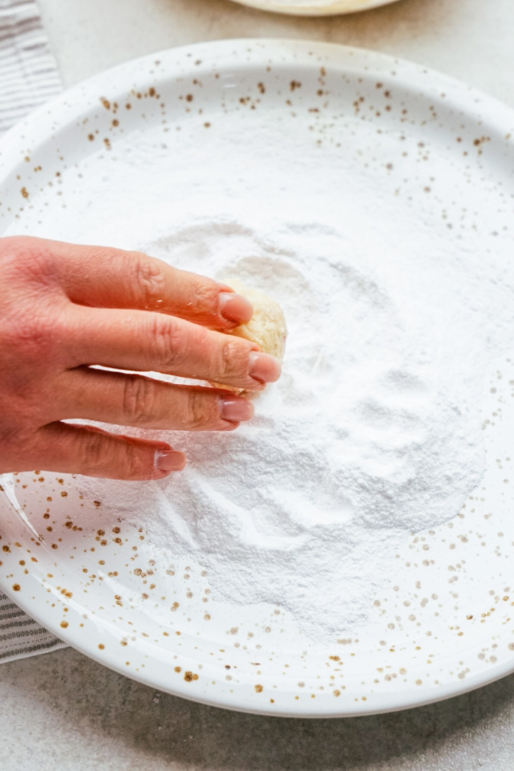 woman's hand rolling cookie dough ball in powdered sugar
