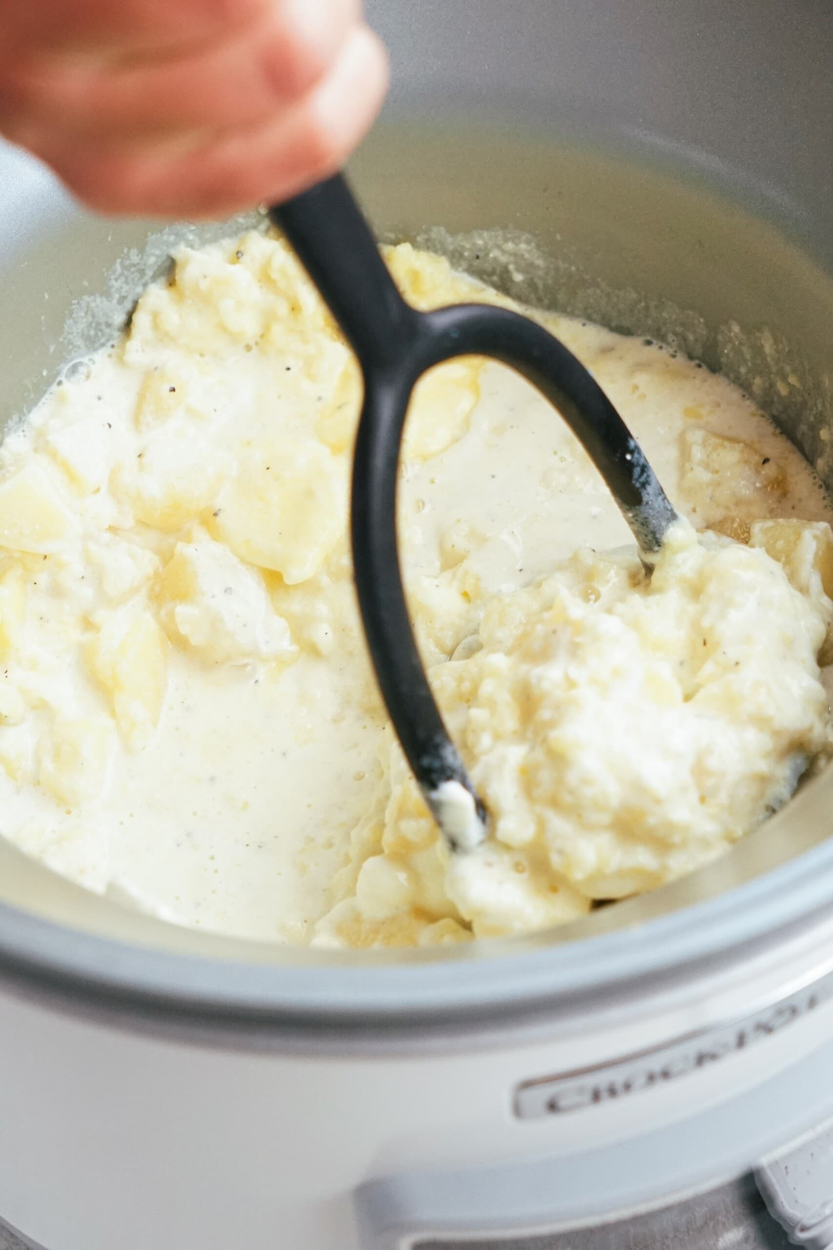 potato masher mashing potatoes in a crockpot