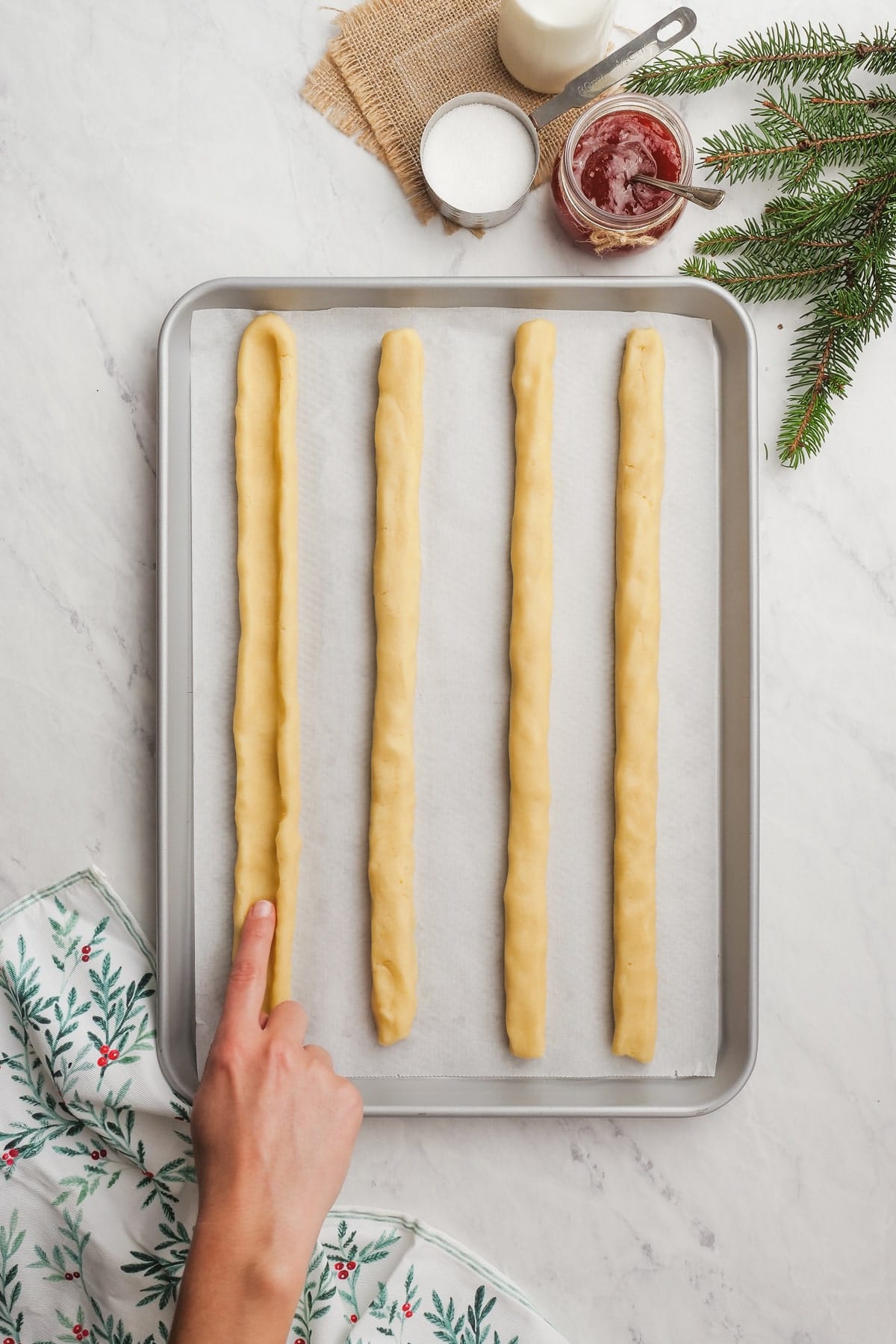 christmas shortbread dough on a baking sheet with womans hand making a well down the strip of dough