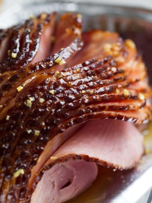 Close-up of a sliced glazed ham with visible seasoning on top.