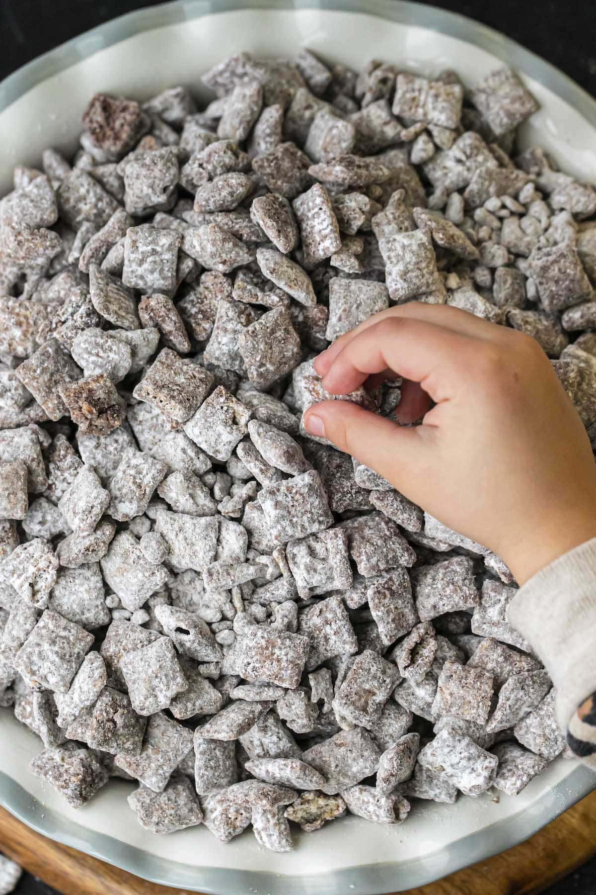 puppy chow in bowl with child's hand grabbing a piece