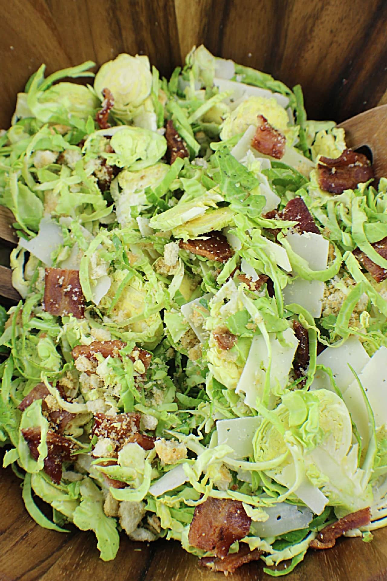 Brussels Sprouts Caesar Salad ingredients mixed together in wooden salad bowl
