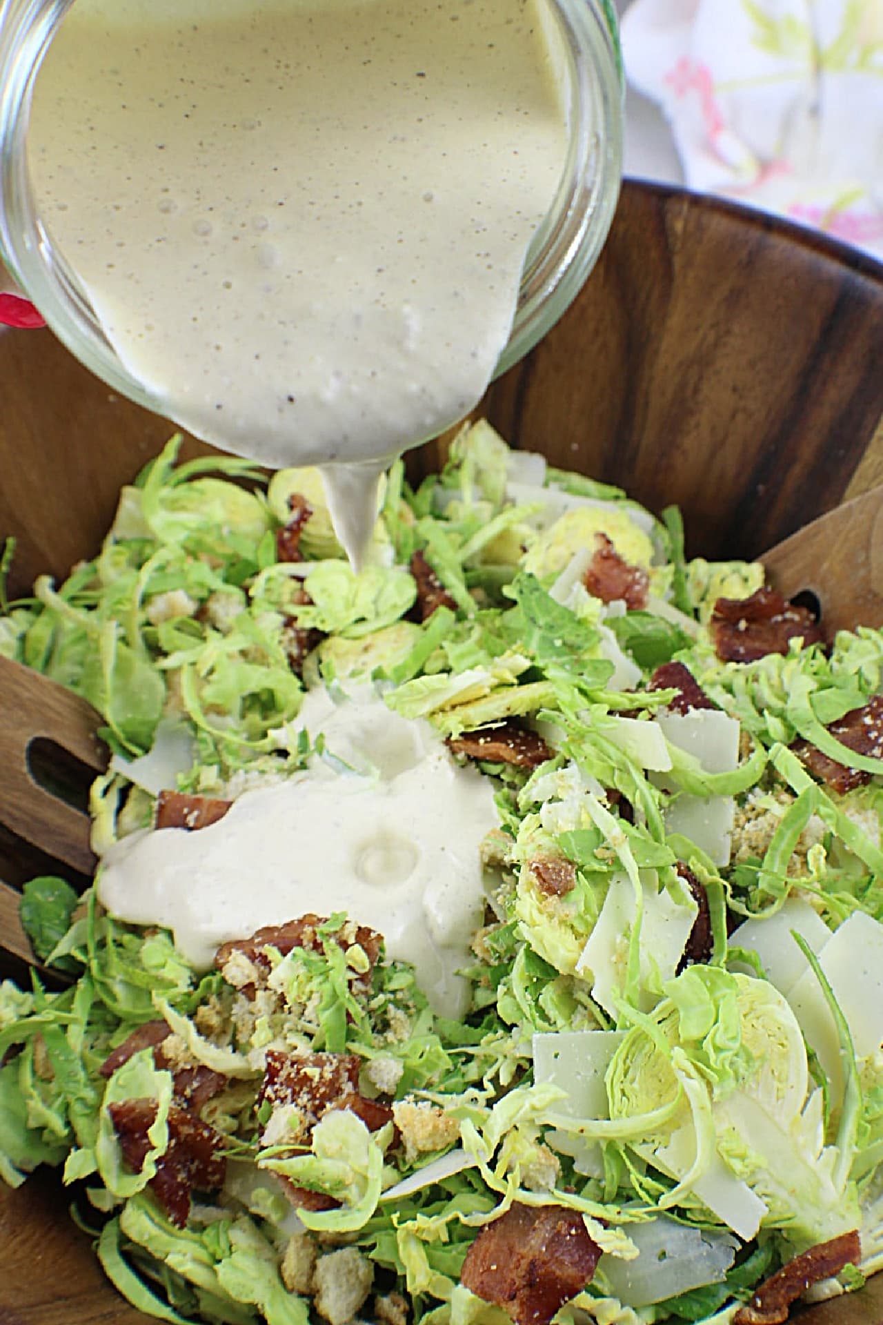 Caesar Dressing being poured over Brussels Sprouts Caesar Salad ingredients