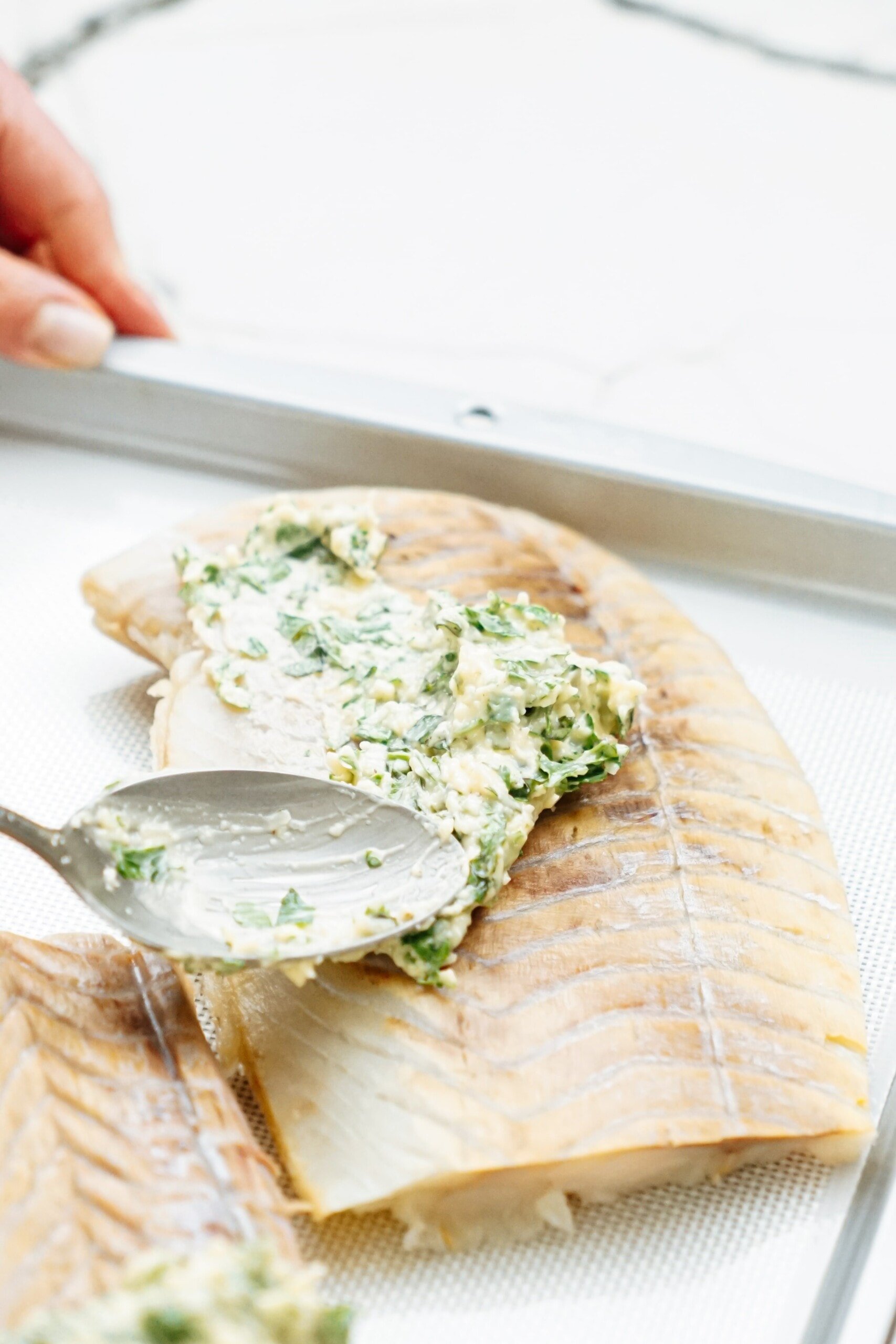spoon smearing parmesan herb mixture over fish fillets