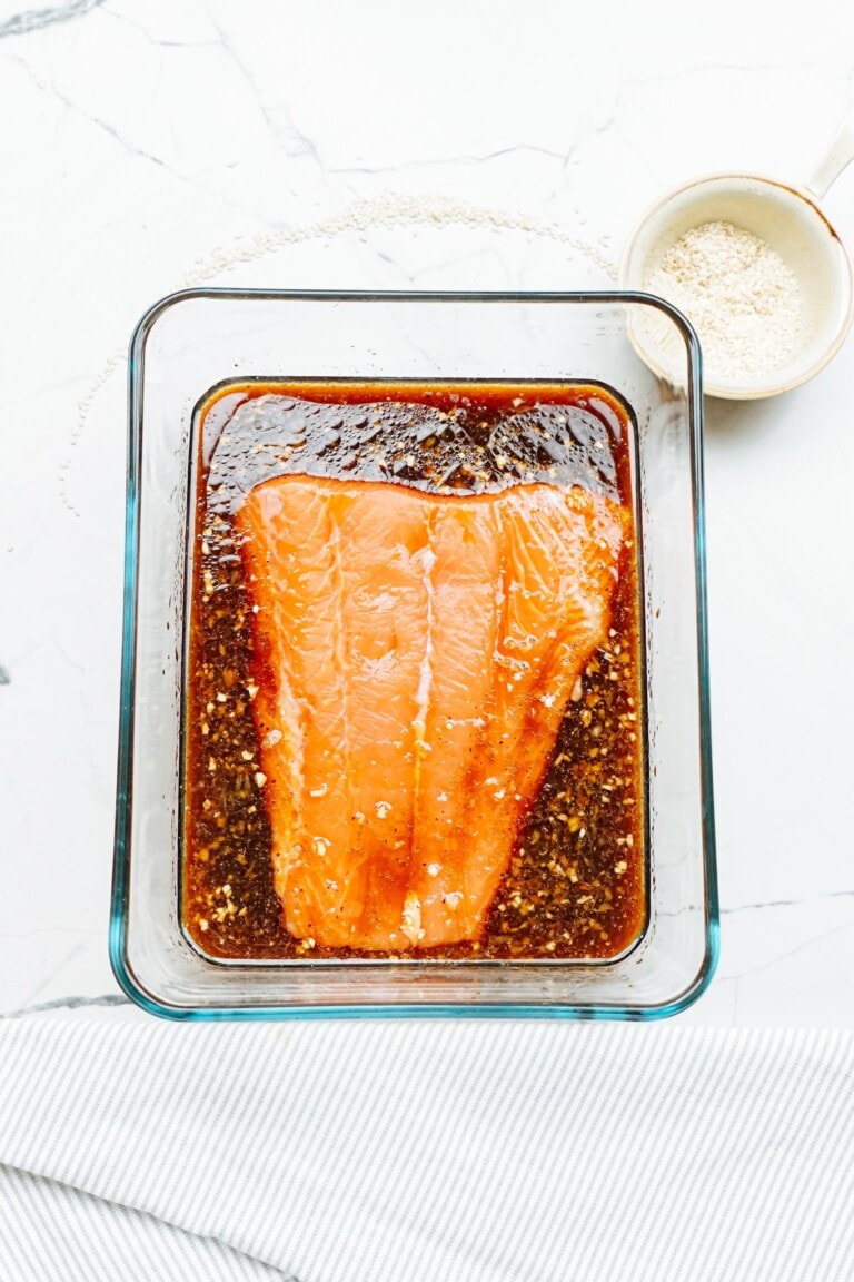 A salmon fillet in a glass dish with sauce.