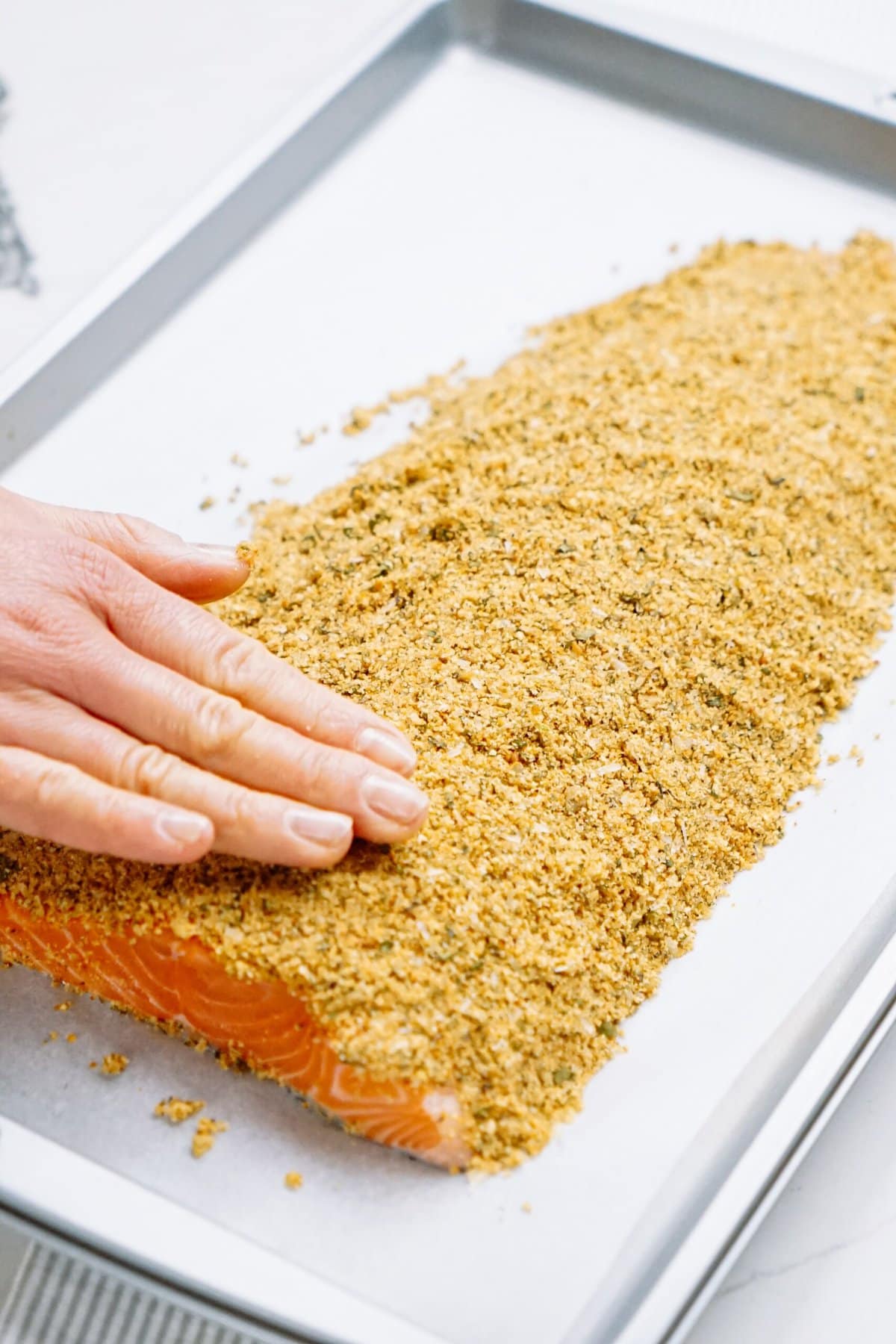 woman's hand patting bread crumbs onto salmon