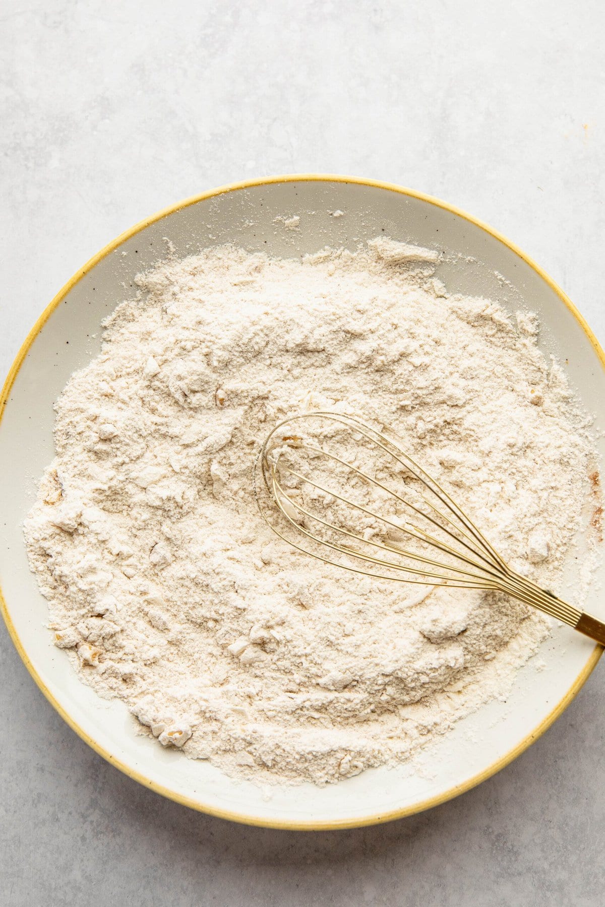 A whisk rests in a bowl of flour on a light-colored surface, ready to whip up a batch of delicious Morning Glory Muffins.