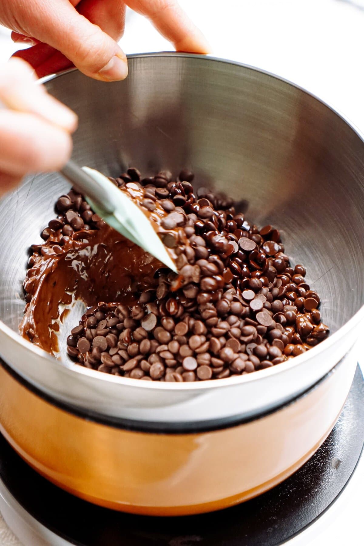 A person stirring chocolate chips in a double boiler to melt them.