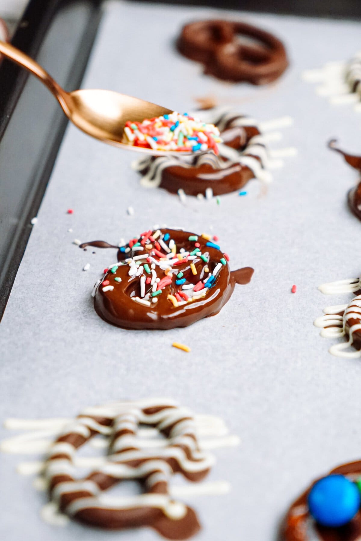 Chocolate covered pretzels with sprinkles on a baking sheet.