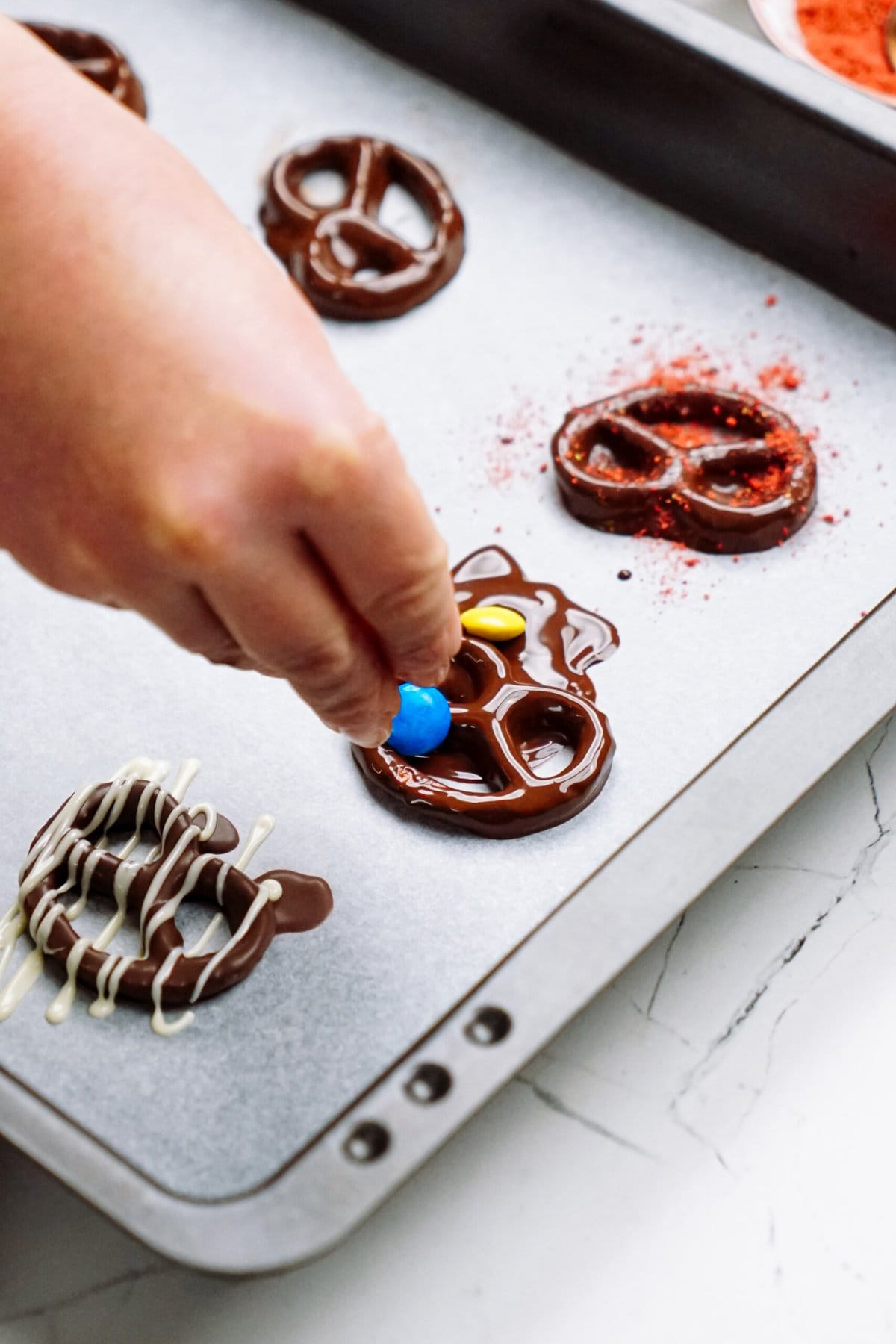 A person is putting m&M's on a chocolate covrered pretzel on a baking sheet.