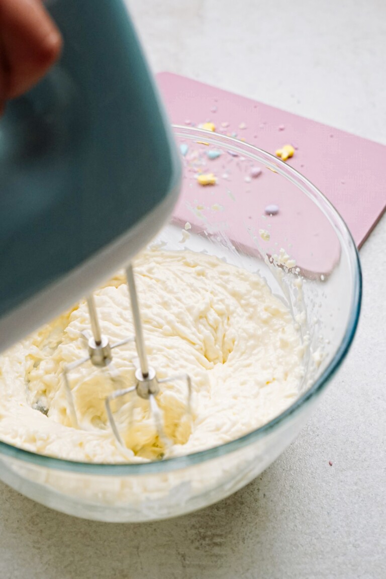 Mixing frosting in a glass bowl with an electric hand mixer.