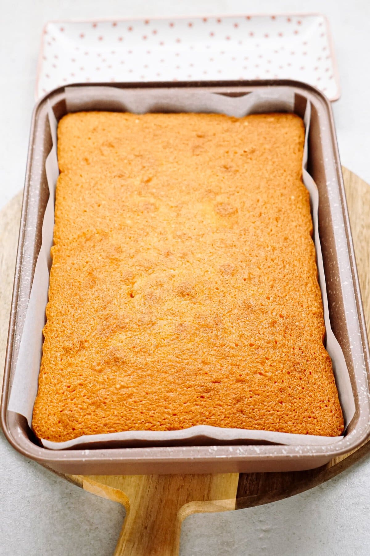 Freshly baked sponge cake in a rectangular baking dish on a wooden board.