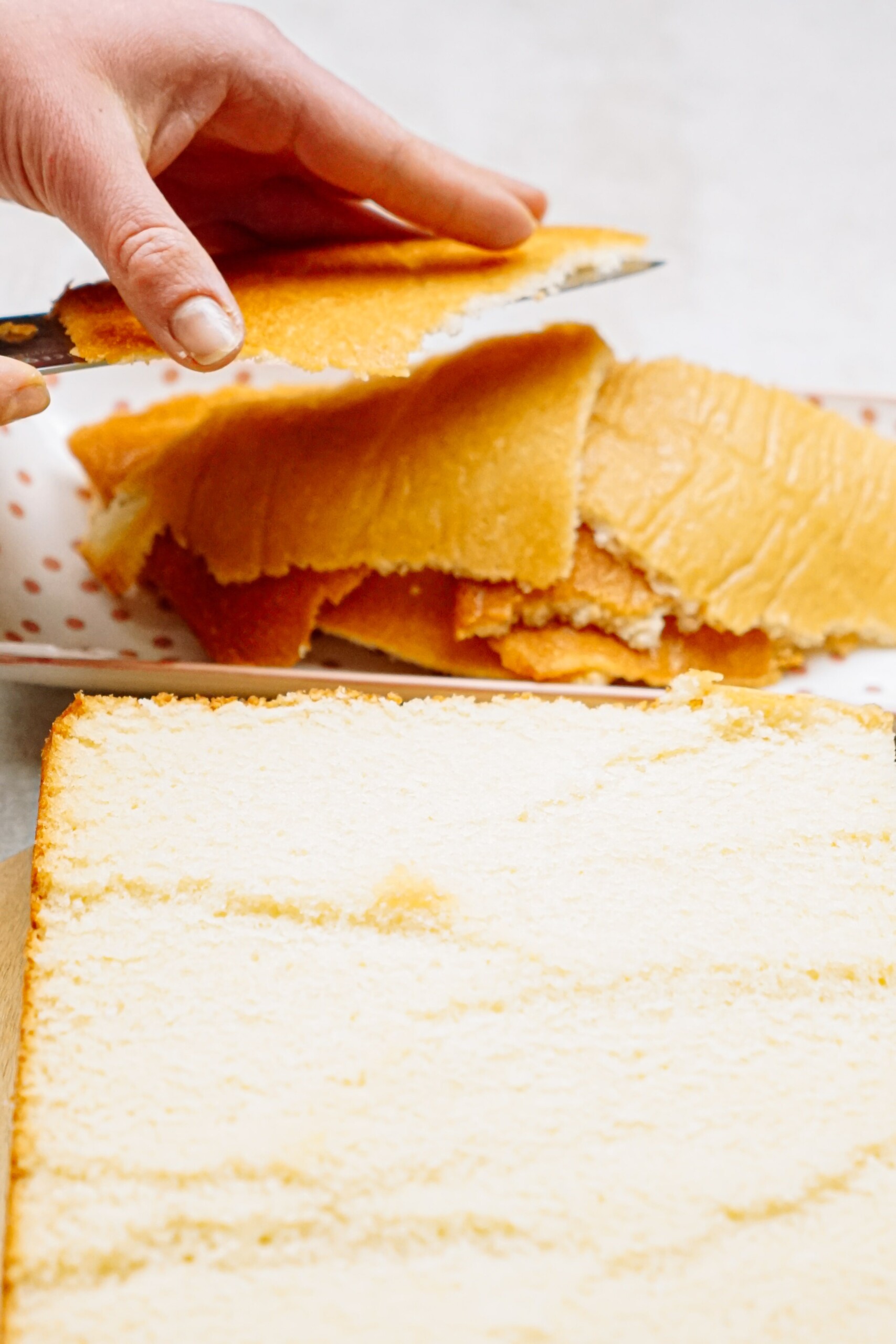 Trimming the top of a yellow cake to create a flat, even surface.