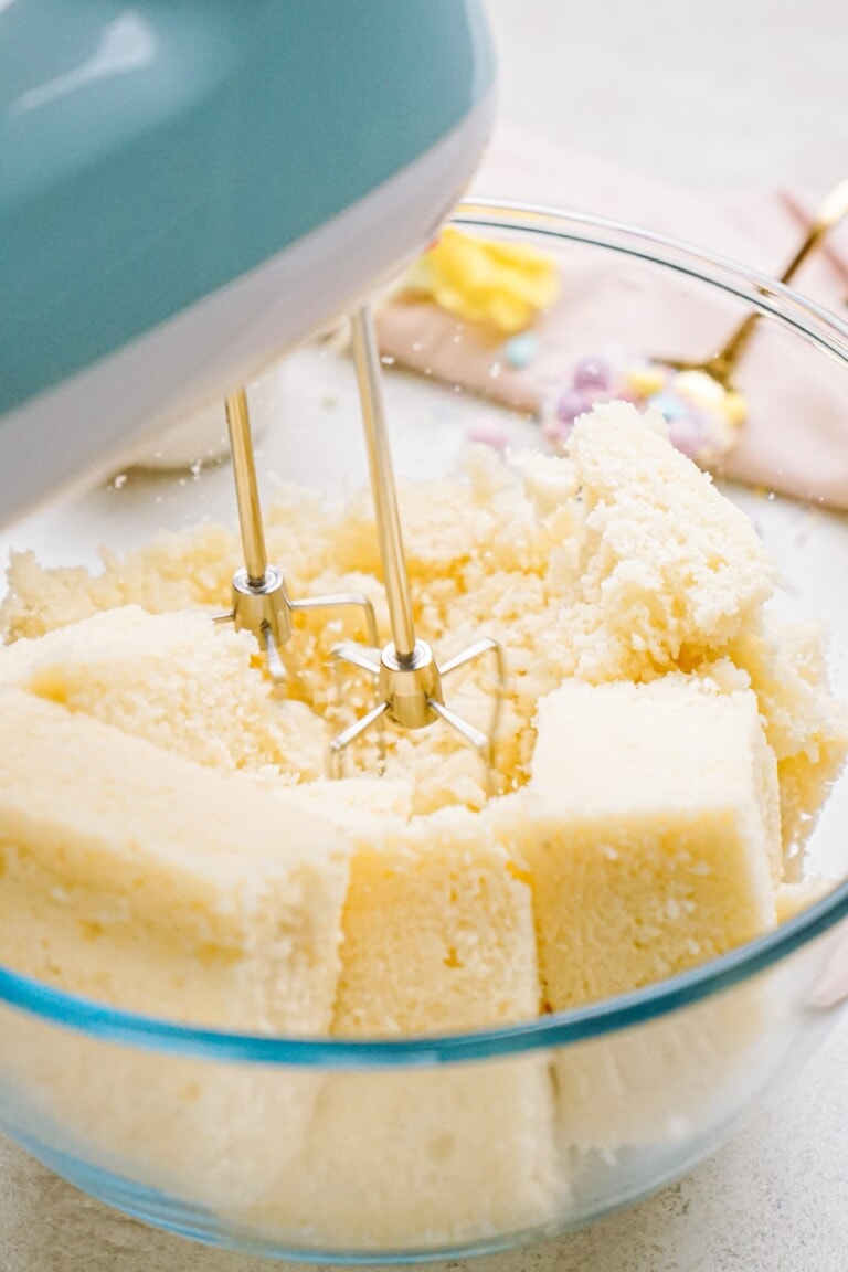 Electric mixer whisking cake squares in a glass bowl.