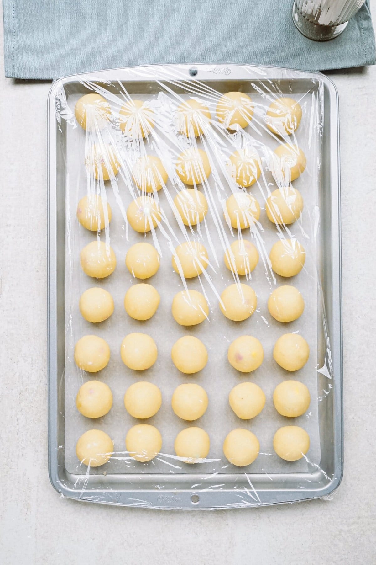 Rows of round cake balls on a tray, covered with plastic wrap.