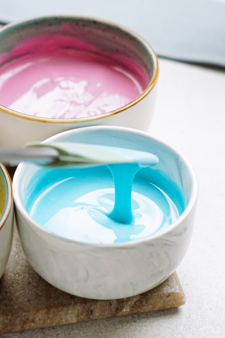 Bowls of blue and pink melted candy coating with a paintbrush.