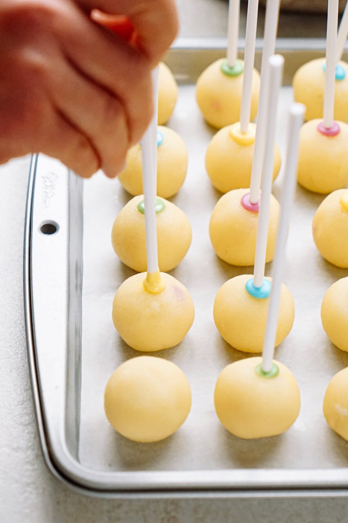 Inserting sticks into yellow cake balls on a baking sheet.