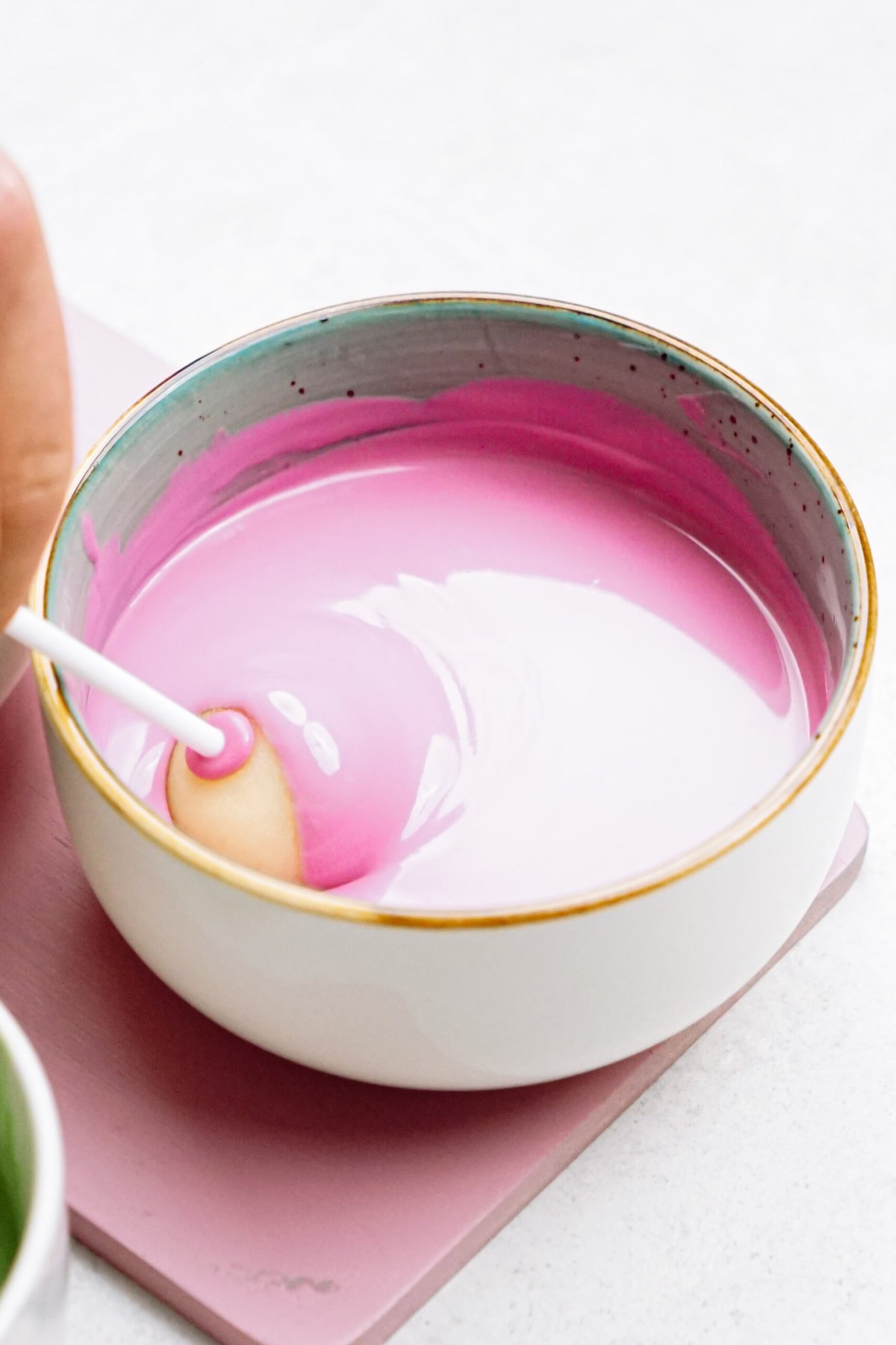 A hand dipping a cake pop into a bowl of pink icing.