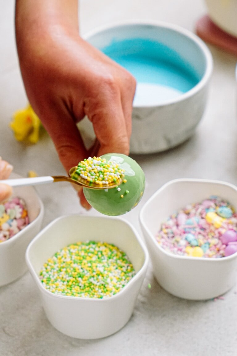 Decorating an egg with vibrant sprinkles over a bowl of colorful candy toppings.