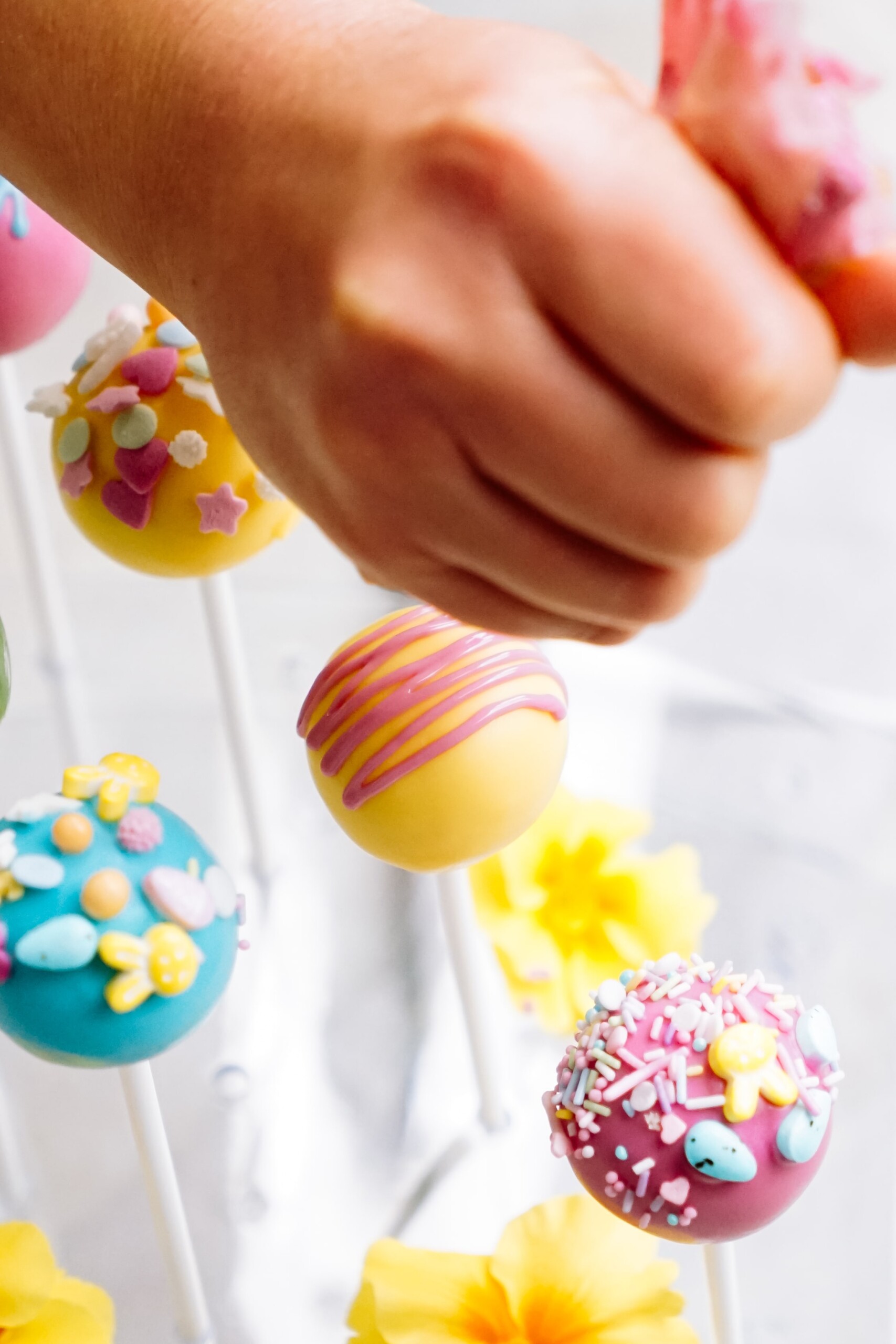 A hand selecting a colorful cake pop from a bouquet of assorted, decorated cake pops.