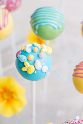 Colorful cake pops decorated with various candies and icing on a blurred background.