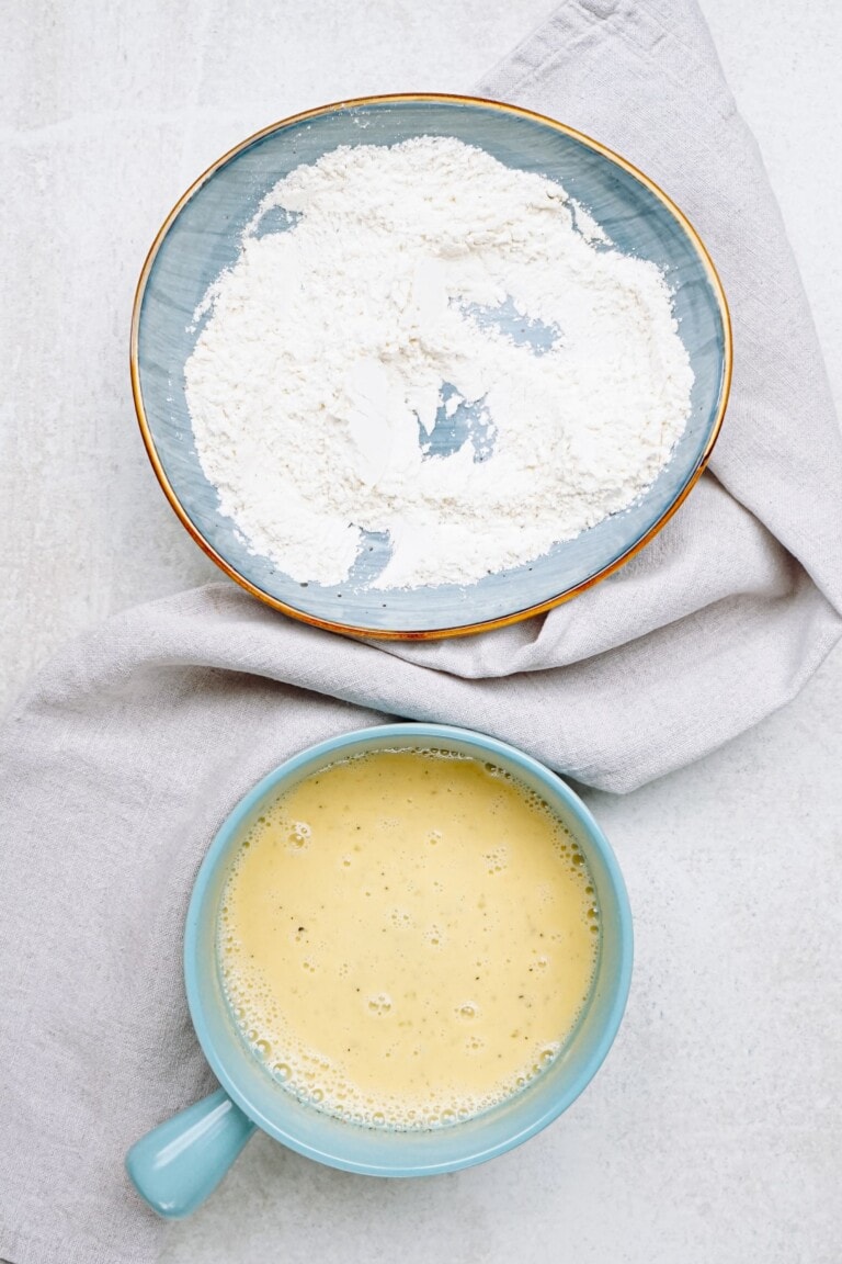 A bowl of flour next to a bowl of milk and egg.