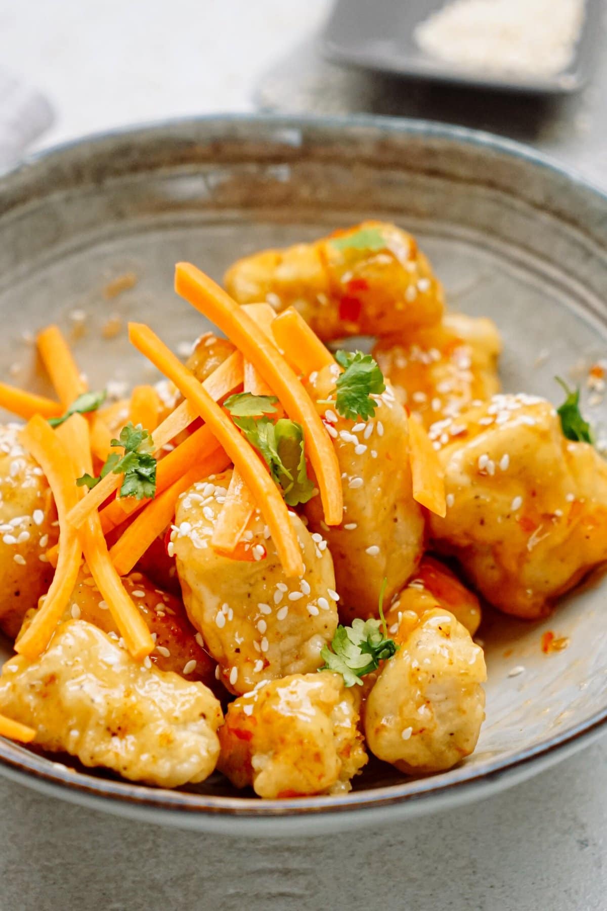 A bowl of asian chicken with carrots and sesame seeds.