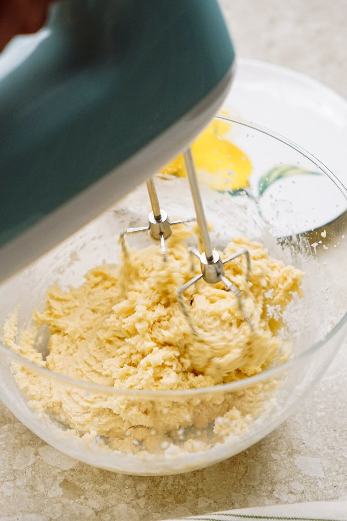 Electric mixer beating eggs and flour in a glass bowl for baking preparation.