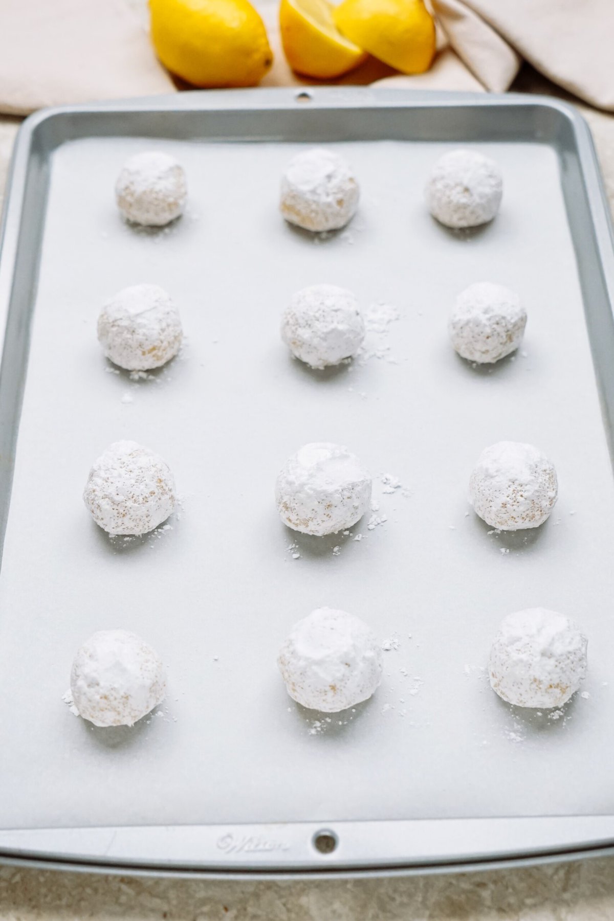 A baking sheet with powdered sugar-dusted cookie dough balls ready for baking.