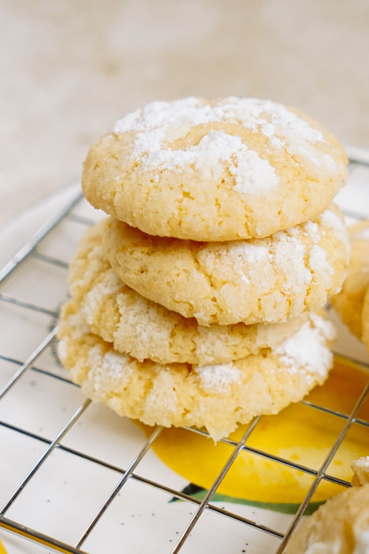 A stack of lemon crinkle cookies dusted with powdered sugar on a cooling rack.