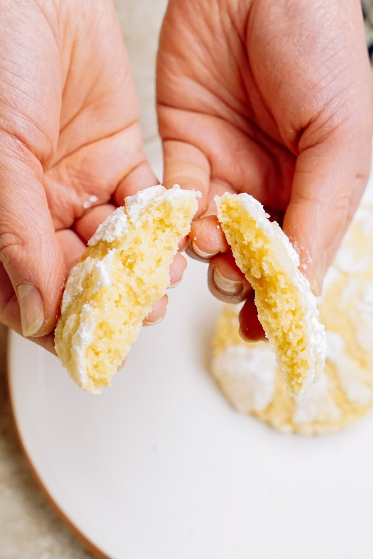 Hands breaking a powdered sugar-coated cookie in half to reveal the inside.