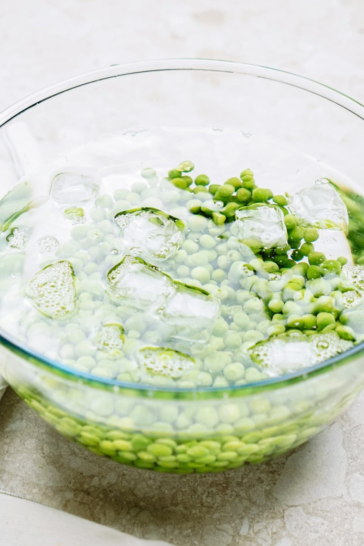 Pea salad soaking in water with ice cubes in a glass bowl.
