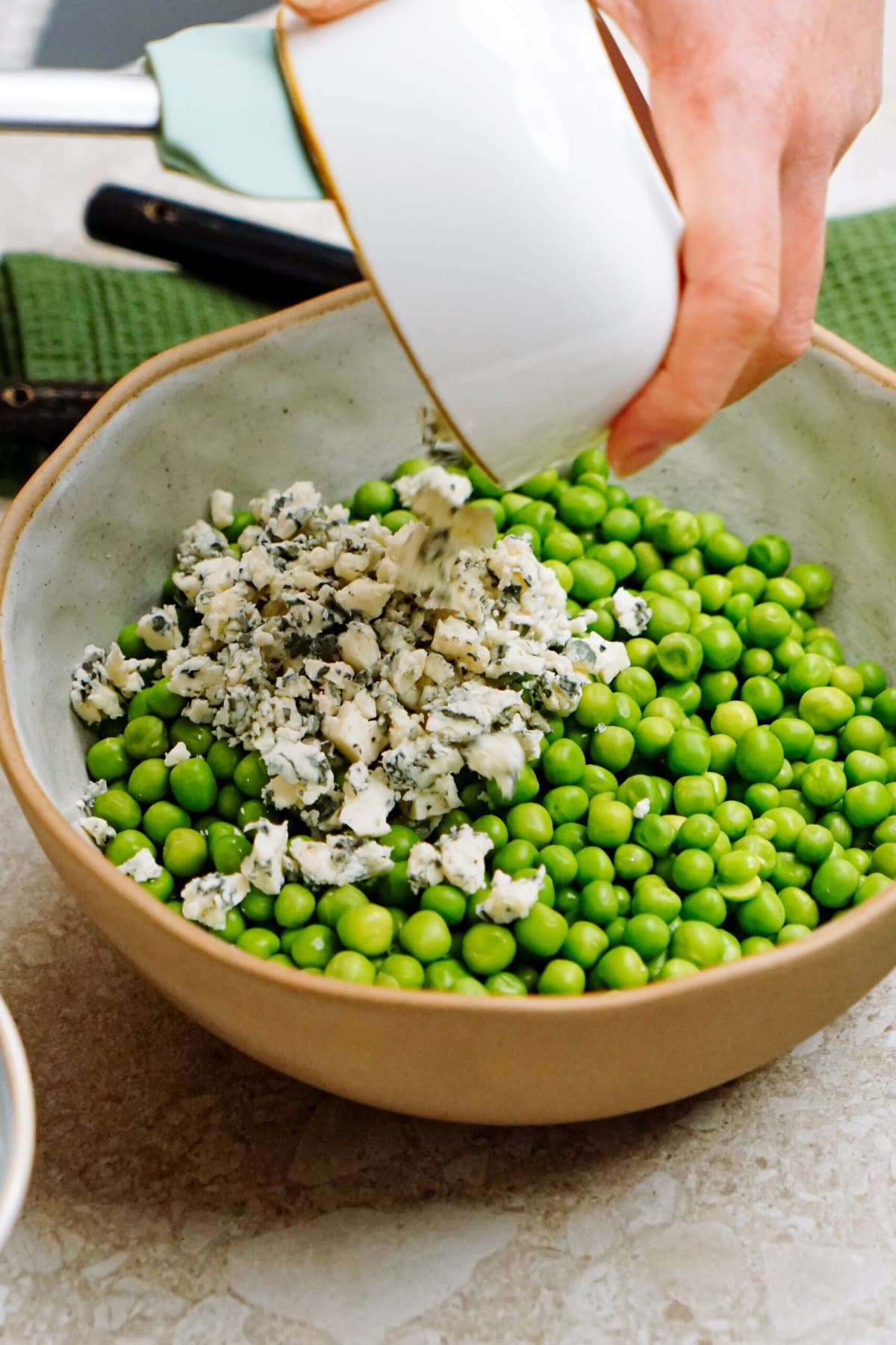 Pouring crumbled cheese onto a bowl of green pea salad.