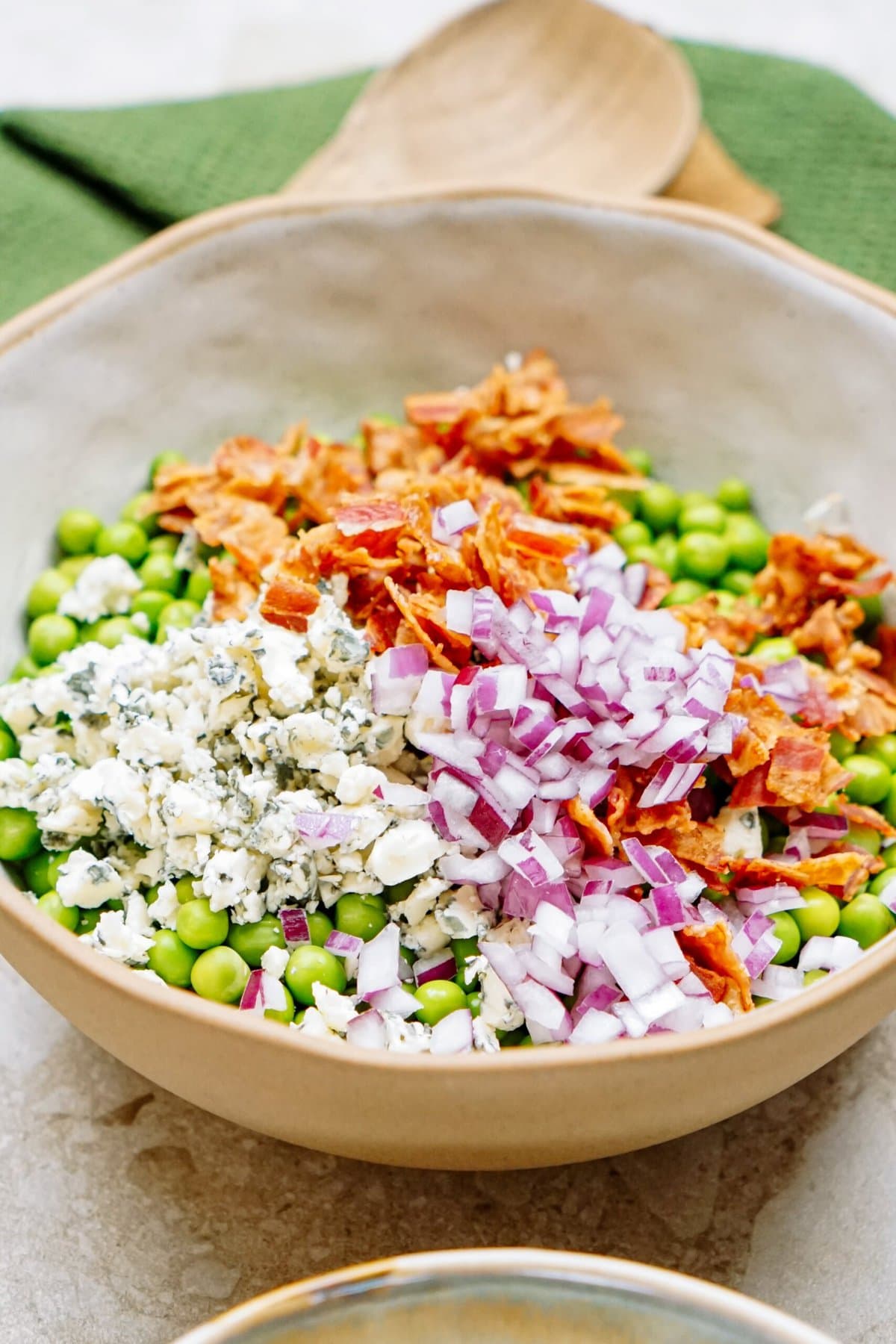 A bowl of pea salad containing peas, chopped red onions, crumbled cheese, and bacon bits.
