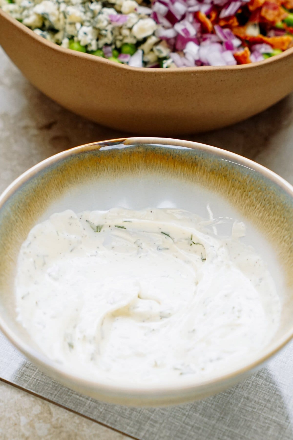 A bowl of creamy dill sauce with a pea salad in the background.