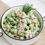 A bowl of pea salad, creamy and garnished with dill.
