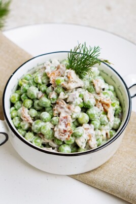 A bowl of pea salad, creamy and garnished with dill.