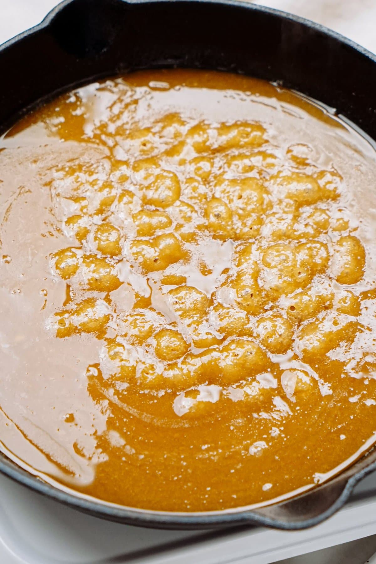 A skillet containing simmering sauce with bubbles forming on the surface.