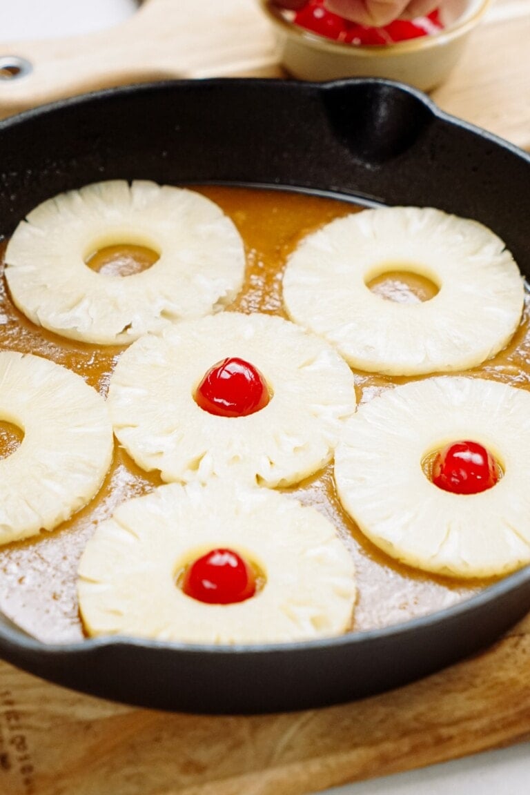 Pineapple slices with cherries in the center, cooking in a skillet.