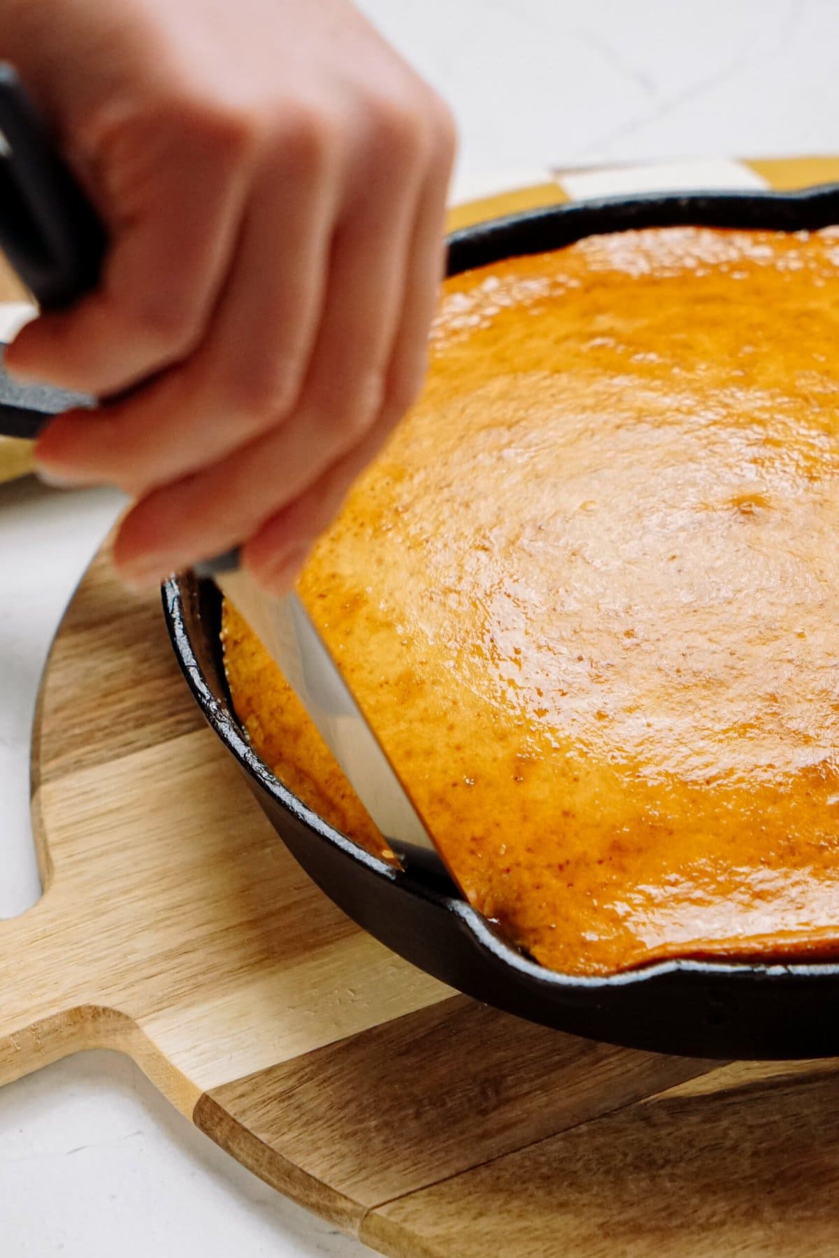 A person slicing a golden-brown upside down cake in a cast-iron skillet.